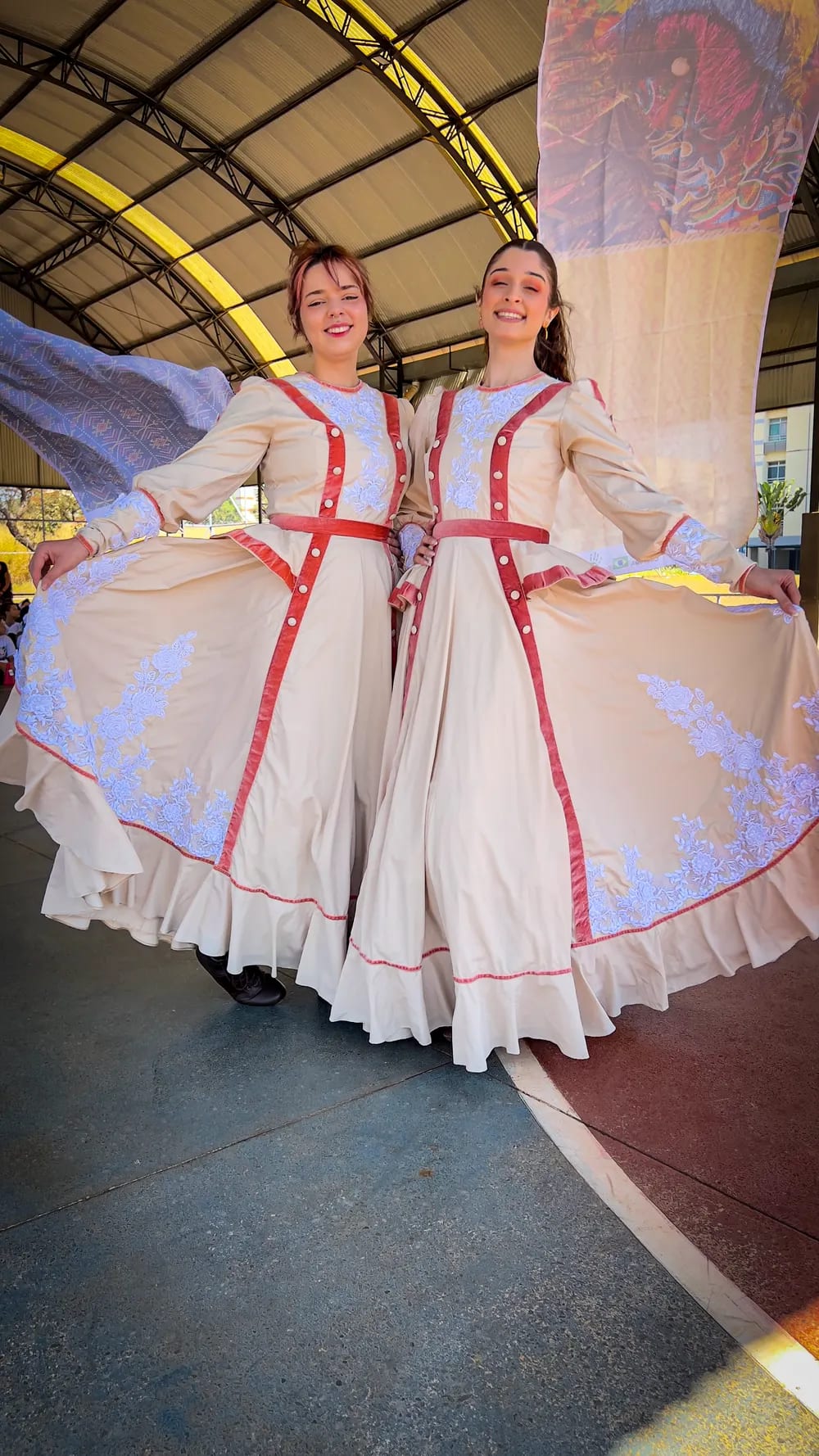 Dançarina adulta em vestido de prenda branco com detalhes vermelhos, no centro da quadra